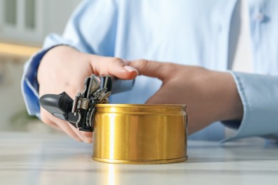 Photo of Woman opening tin with can opener at white marble table, closeup