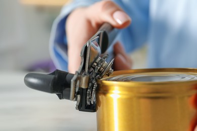 Photo of Woman opening tin with can opener at white marble table, closeup