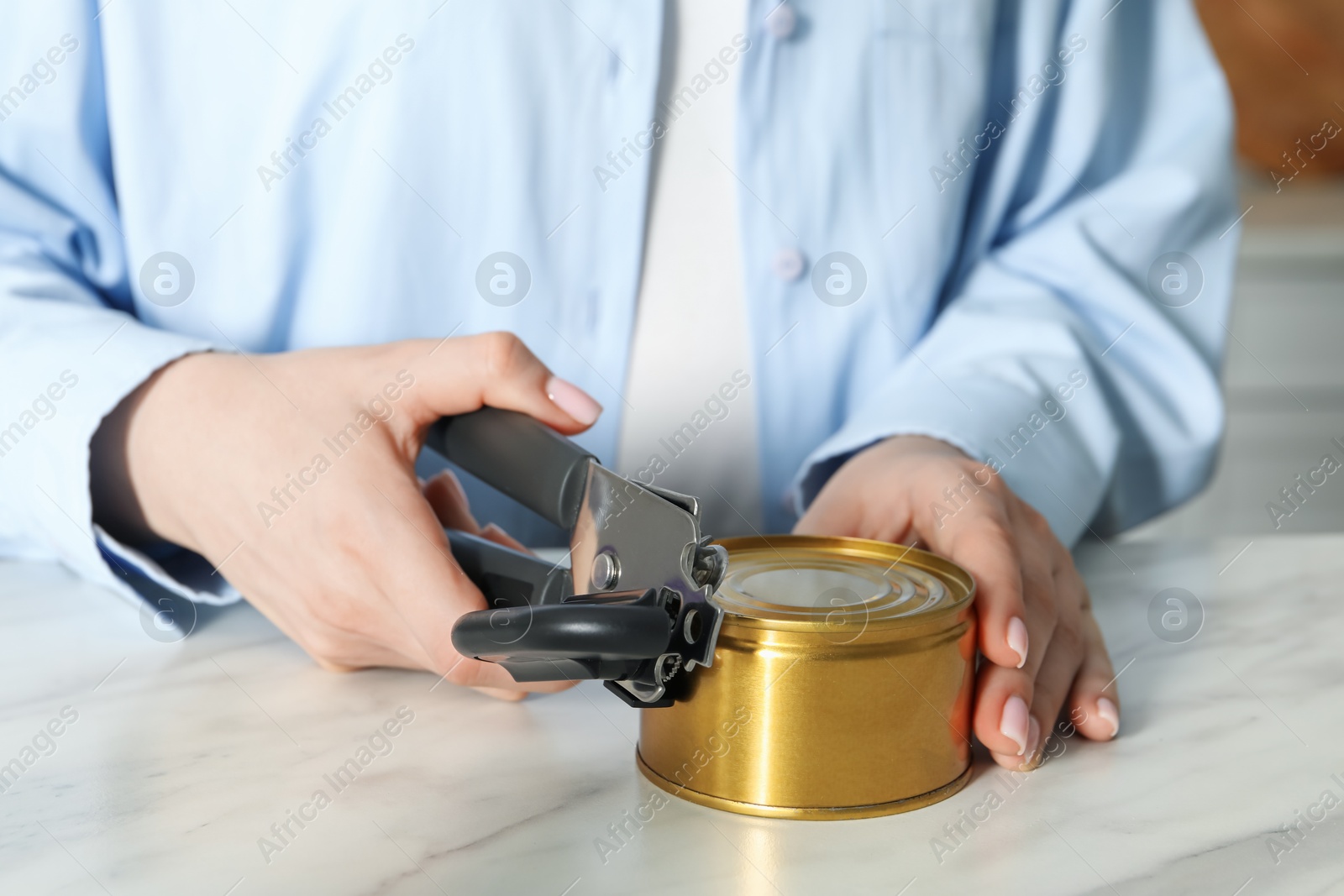 Photo of Woman opening tin with can opener at white marble table, closeup