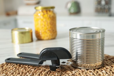 Photo of Can opener and tin on white table indoors, closeup