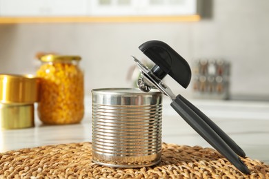Photo of Can opener and tin on white table indoors, closeup