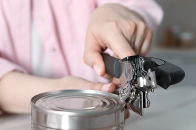 Photo of Woman opening tin with can opener at white table, closeup