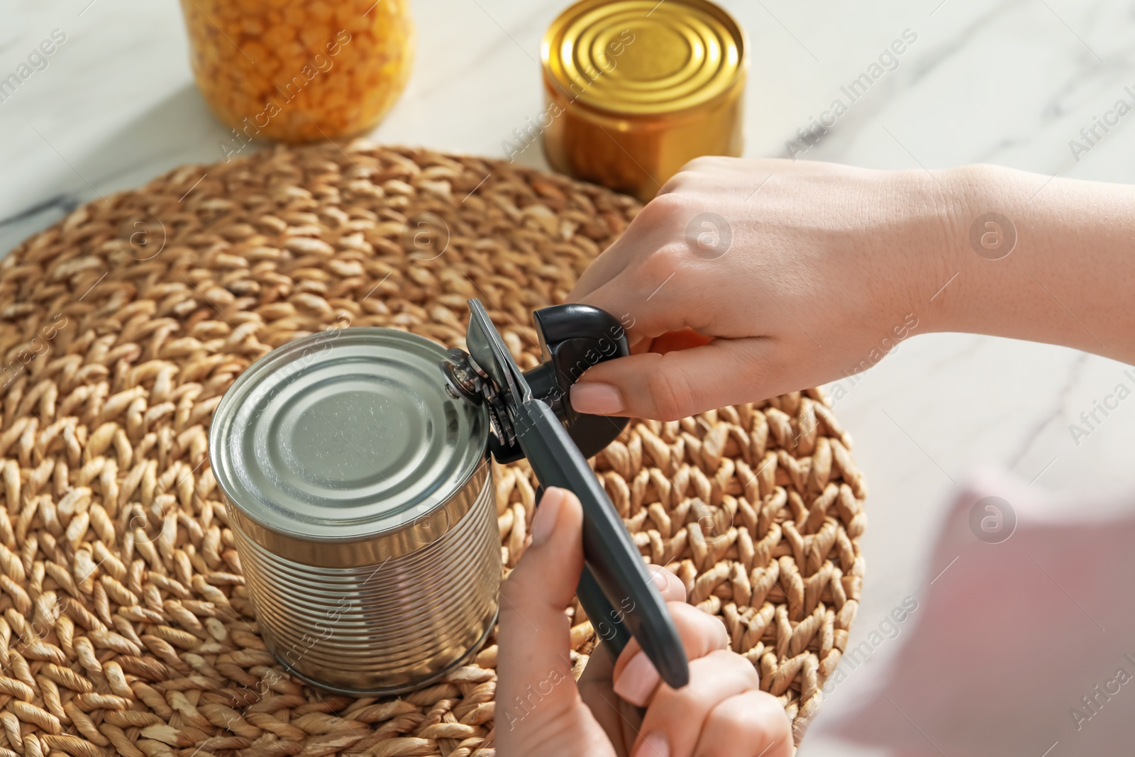 Woman opening tin with can opener at white marble table, closeup Photo of Woman opening tin with can opener at white marble table, closeup
