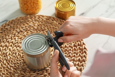 Photo of Woman opening tin with can opener at white marble table, closeup