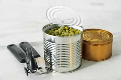 Photo of Can opener and tin with peas on white marble table, closeup