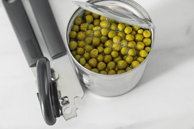Photo of Can opener and tin with peas on white marble table, above view