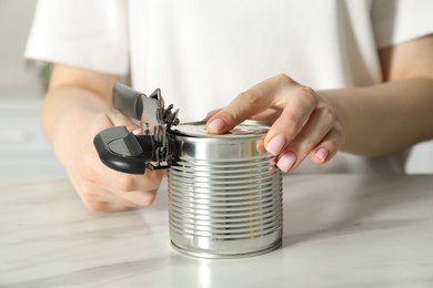 Photo of Woman opening tin with can opener at white table, closeup