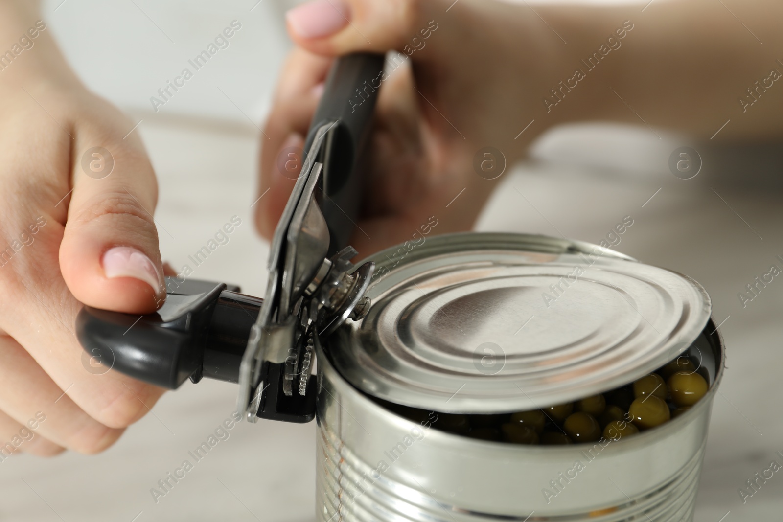 Woman opening tin with can opener at white table, closeup Photo of Woman opening tin with can opener at white table, closeup