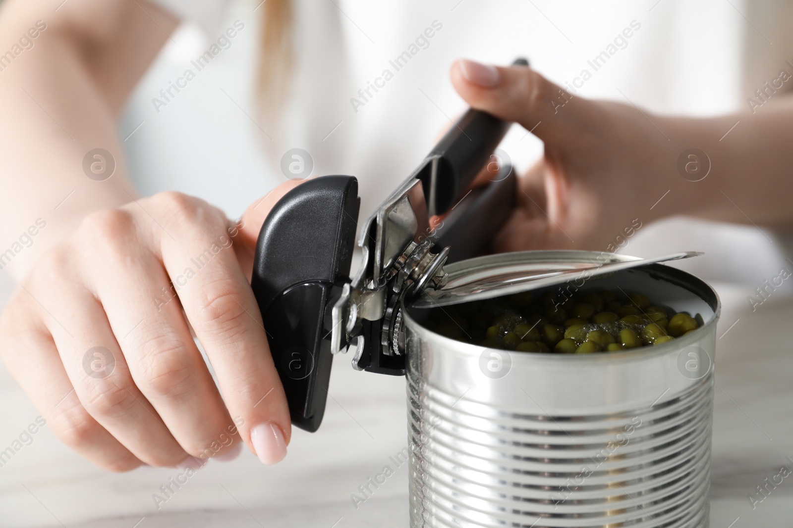 Woman opening tin with can opener at white table, closeup Photo of Woman opening tin with can opener at white table, closeup