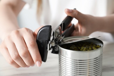 Photo of Woman opening tin with can opener at white table, closeup