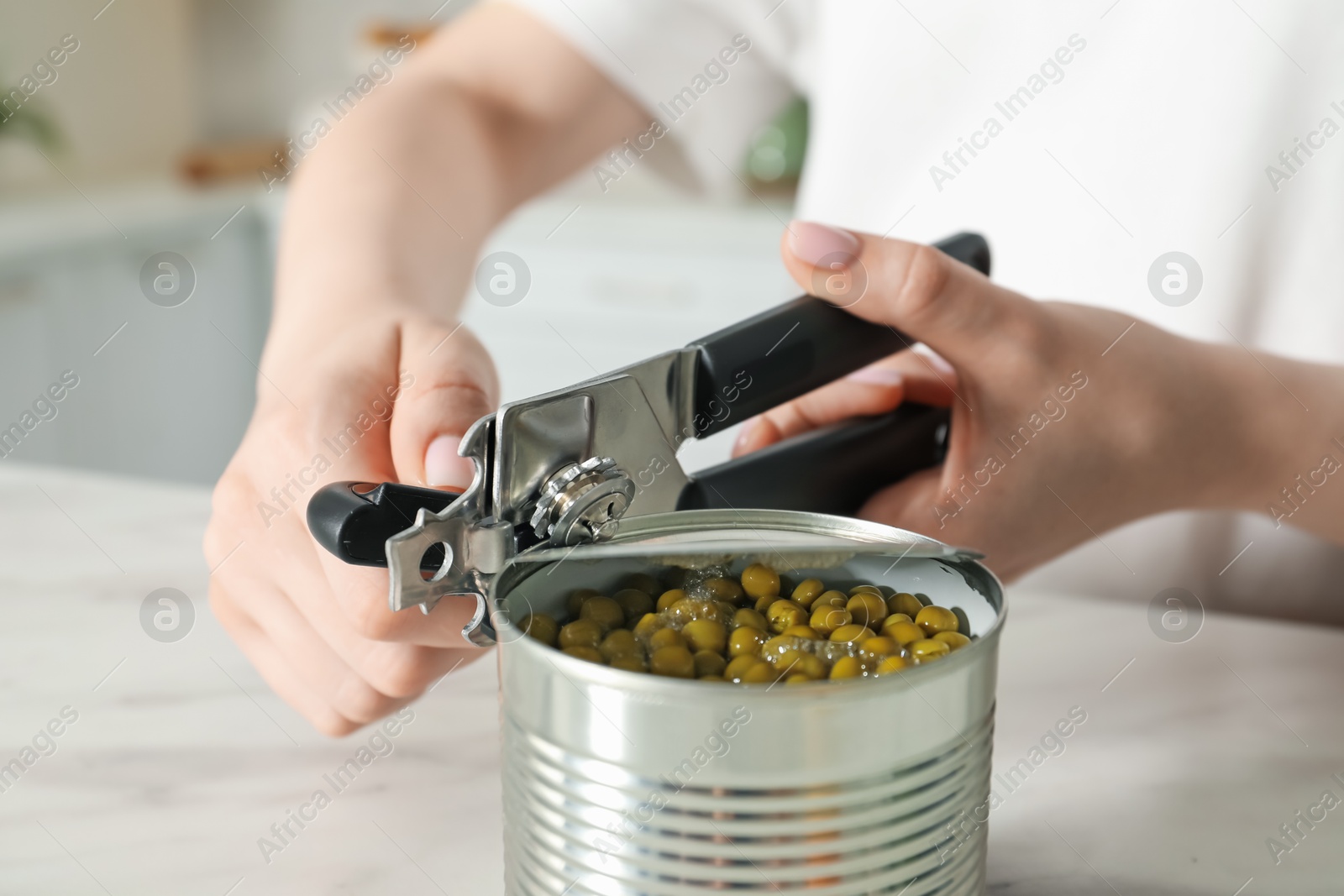 Woman opening tin with can opener at white table, closeup Photo of Woman opening tin with can opener at white table, closeup