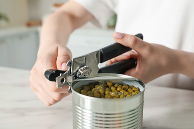 Photo of Woman opening tin with can opener at white table, closeup