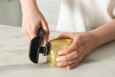 Photo of Woman opening tin with can opener at white table, closeup