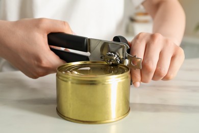 Photo of Woman opening tin with can opener at white table, closeup
