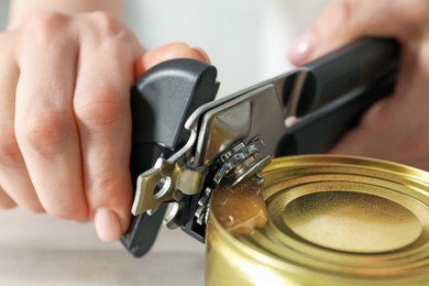 Photo of Woman opening tin with can opener at white table, closeup