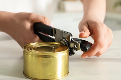 Photo of Woman opening tin with can opener at white table, closeup