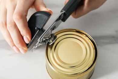 Photo of Woman opening tin with can opener at white table, closeup