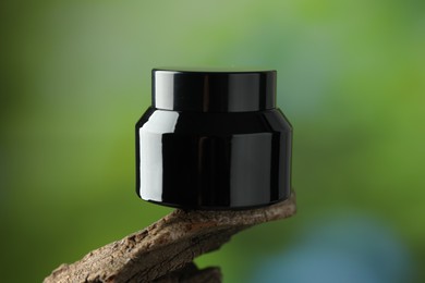 Photo of Jar of body cream on tree branch against blurred background, closeup