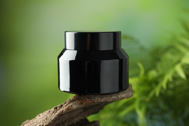Photo of Jar of body cream on tree branch against blurred background, closeup