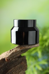 Photo of Jar of body cream on tree branch against blurred background, closeup