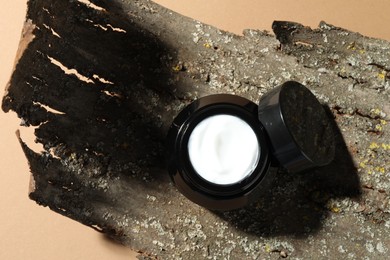 Photo of Jar of body cream and tree bark on beige background, top view