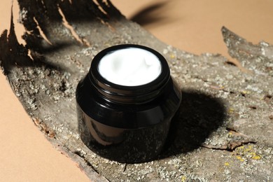 Photo of Jar of body cream and tree bark on beige background, closeup