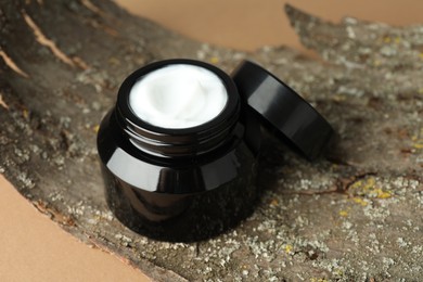 Photo of Jar of body cream and tree bark on beige background, closeup