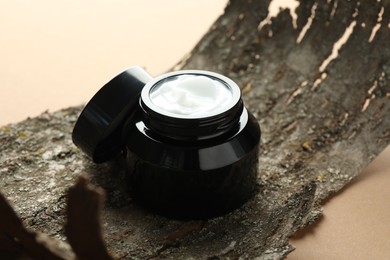Photo of Jar of body cream and tree bark on beige background, closeup