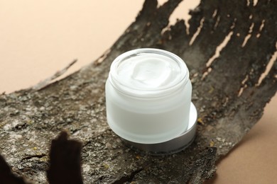 Photo of Jar of body cream and tree bark on beige background, closeup