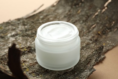 Photo of Jar of body cream and tree bark on beige background, closeup