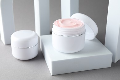 Photo of Stylish presentation of body cream in jars on light grey background, closeup
