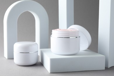 Photo of Stylish presentation of body cream in jars on light grey background, closeup
