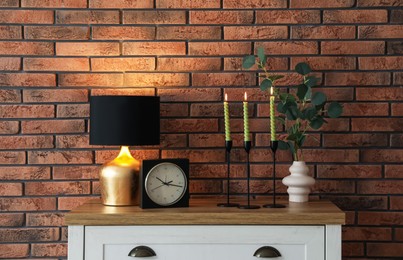 Photo of Candlesticks with burning candles on table near brick wall