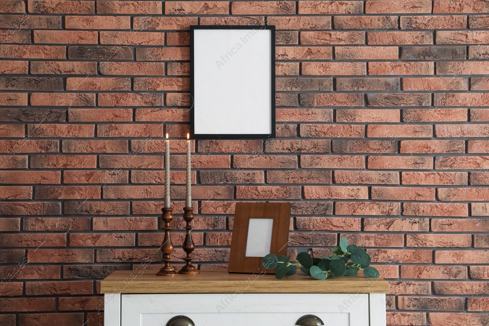 Candlesticks with burning candles on table near brick wall Photo of Candlesticks with burning candles on table near brick wall