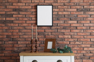 Photo of Candlesticks with burning candles on table near brick wall