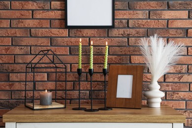 Photo of Candlesticks with burning candles on table near brick wall