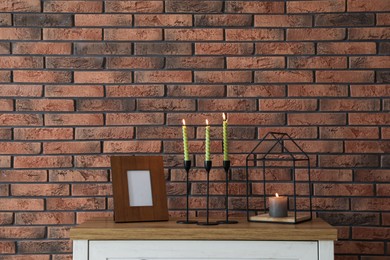 Photo of Candlesticks with burning candles on table near brick wall