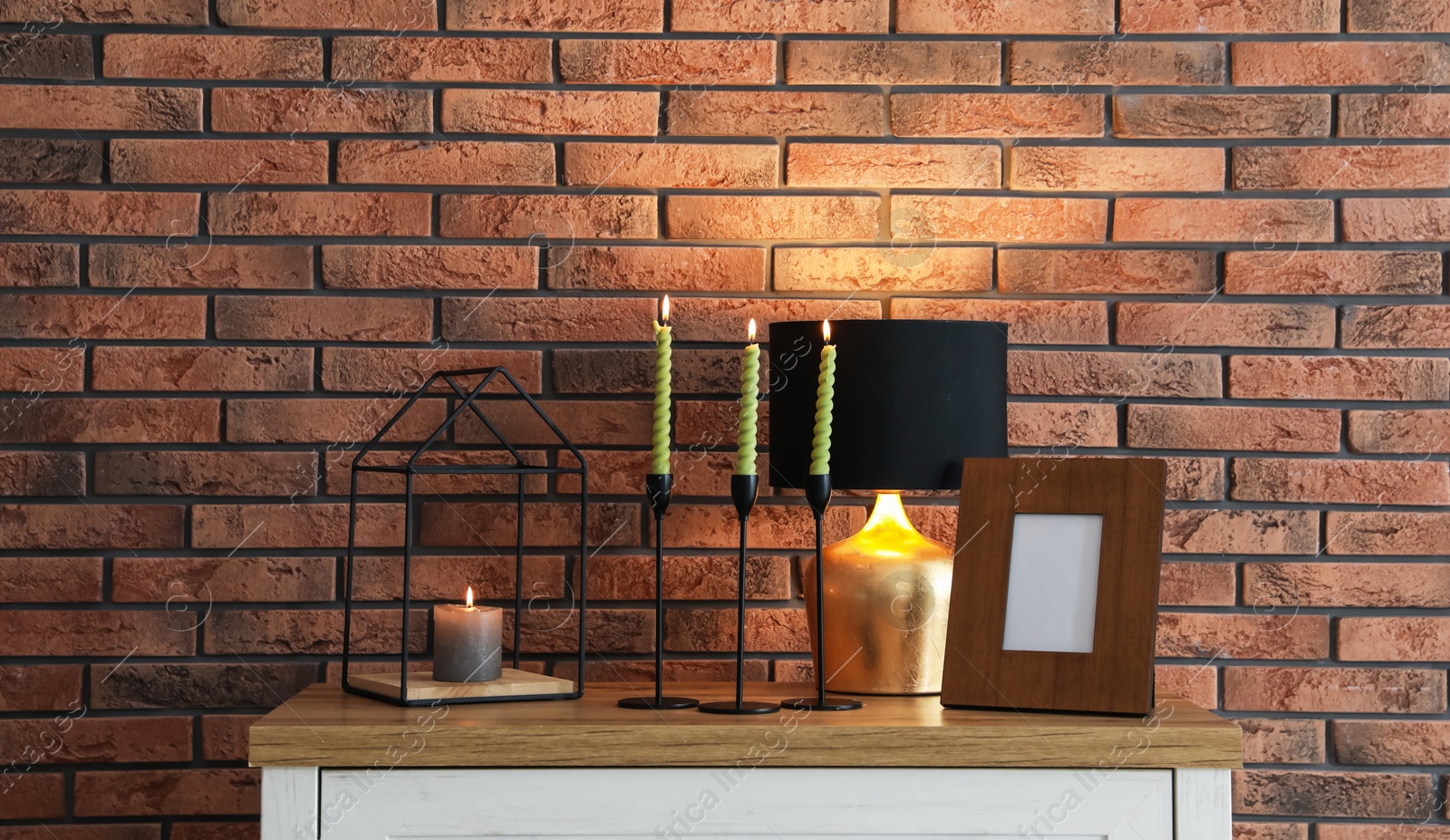 Candlesticks with burning candles on table near brick wall Photo of Candlesticks with burning candles on table near brick wall