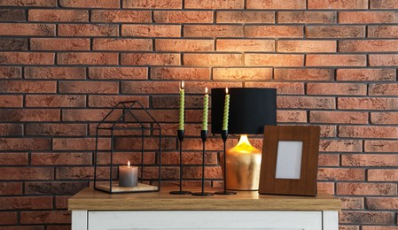 Photo of Candlesticks with burning candles on table near brick wall