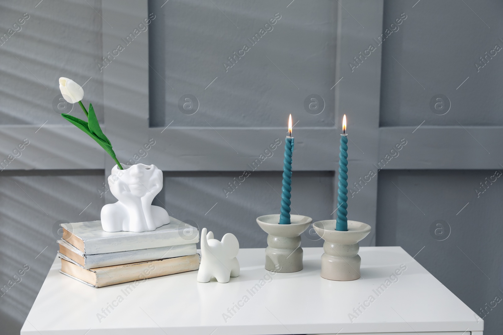 Candlesticks with burning candles on table near grey wall Photo of Candlesticks with burning candles on table near grey wall