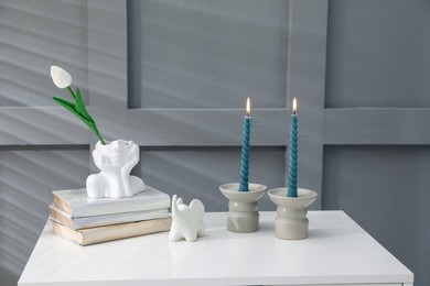 Photo of Candlesticks with burning candles on table near grey wall