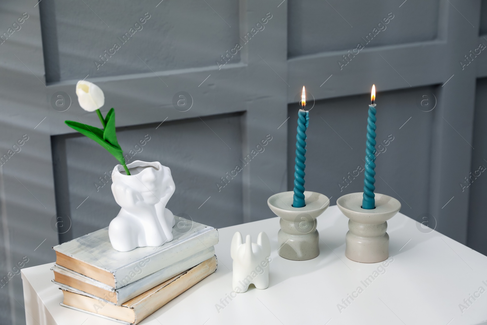 Candlesticks with burning candles on table near grey wall Photo of Candlesticks with burning candles on table near grey wall
