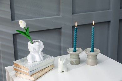 Photo of Candlesticks with burning candles on table near grey wall