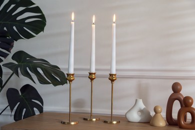 Photo of Candlesticks with burning candles on table near white wall