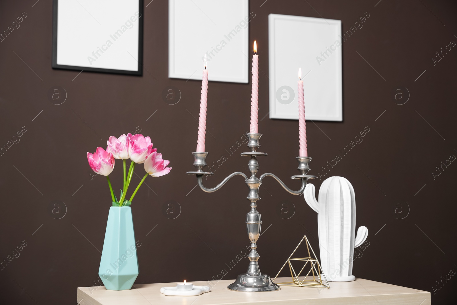 Elegant candlestick with burning candles and decor on table near brown wall Photo of Elegant candlestick with burning candles and decor on table near brown wall