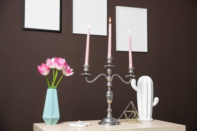 Photo of Elegant candlestick with burning candles and decor on table near brown wall