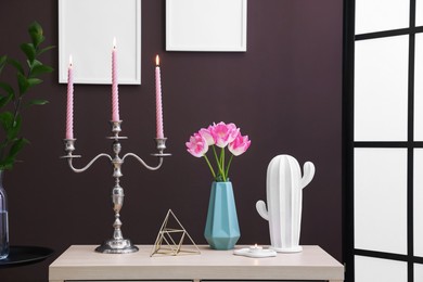 Photo of Elegant candlestick with burning candles and decor on table near brown wall