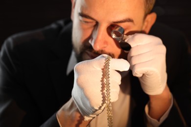 Photo of Appraiser with loupe evaluating luxury jewelry indoors, selective focus