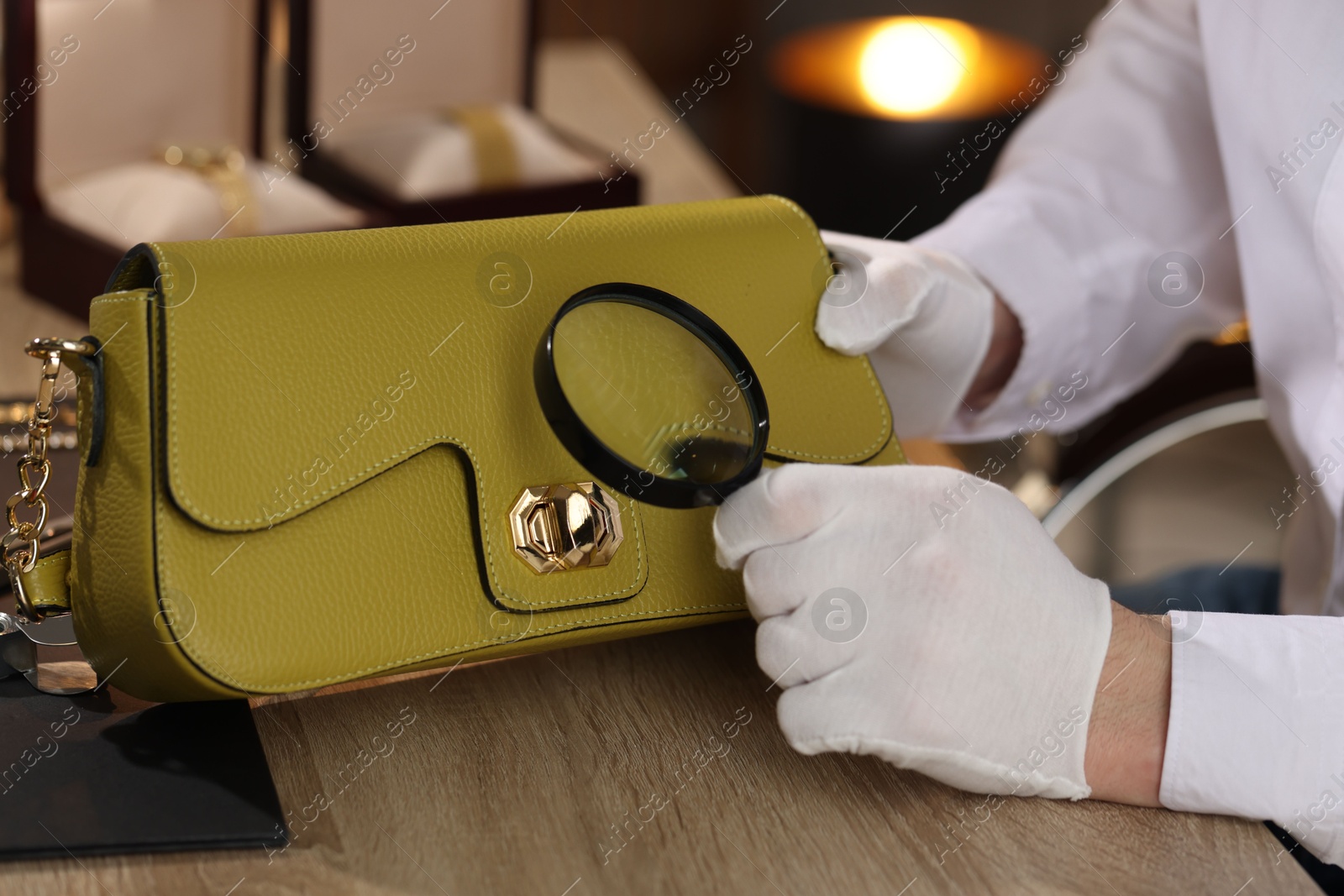 Appraiser with magnifying glass evaluating leather bag at table indoors, closeup Photo of Appraiser with magnifying glass evaluating leather bag at table indoors, closeup