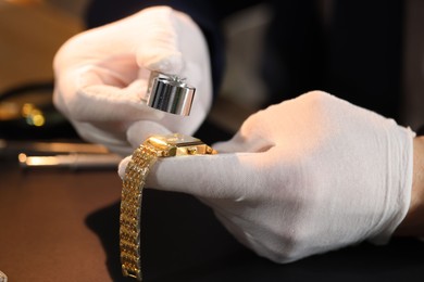 Photo of Appraiser with loupe evaluating luxury wristwatch at table, closeup